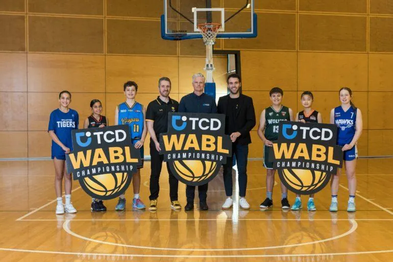 Junior players and officials holding TCD WABL Championship signs on a basketball court