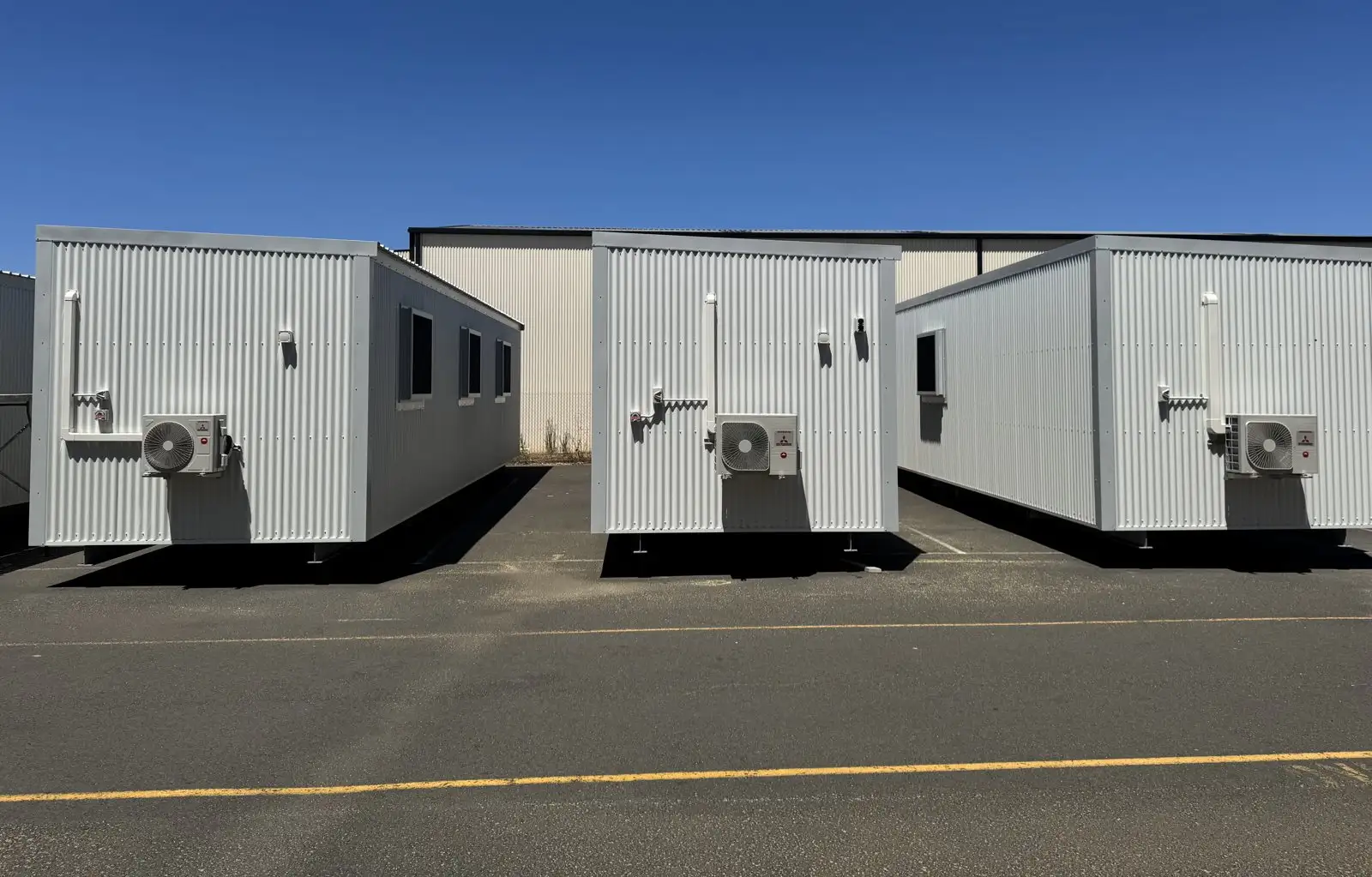 Three white portable buildings with split-system air-conditioners, lined up in a sealed yard